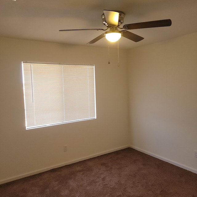 spare room featuring baseboards, dark carpet, and a ceiling fan