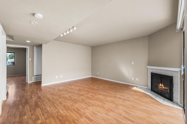 unfurnished living room featuring a tile fireplace, a textured ceiling, light wood-type flooring, baseboards, and visible vents