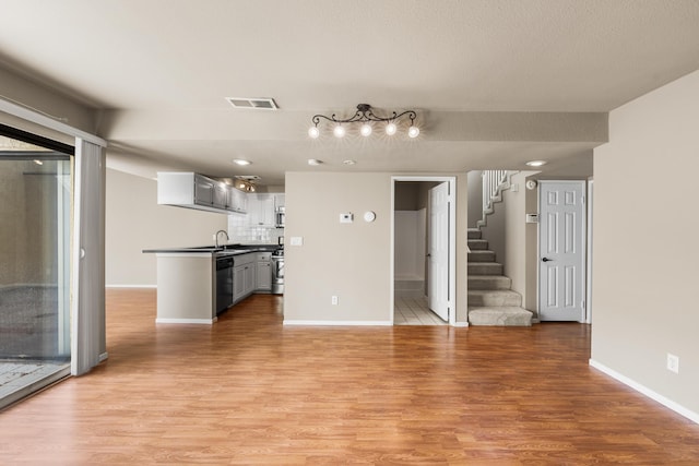unfurnished living room featuring a sink, stairs, light wood-style flooring, and visible vents
