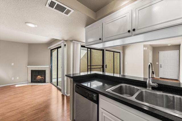 kitchen featuring light wood-type flooring, a sink, visible vents, dishwasher, and a fireplace
