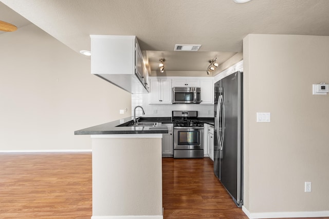 kitchen with a sink, dark countertops, visible vents, a peninsula, and appliances with stainless steel finishes