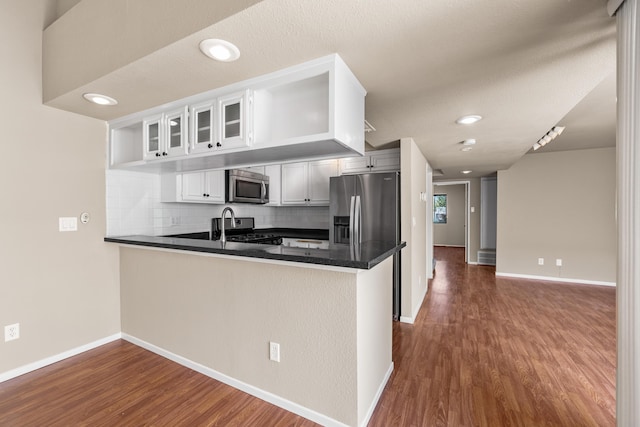 kitchen featuring decorative backsplash, dark wood-style flooring, stainless steel appliances, and a peninsula