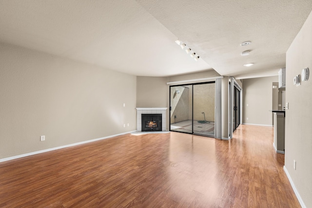 unfurnished living room featuring a tiled fireplace, a textured ceiling, baseboards, and wood finished floors