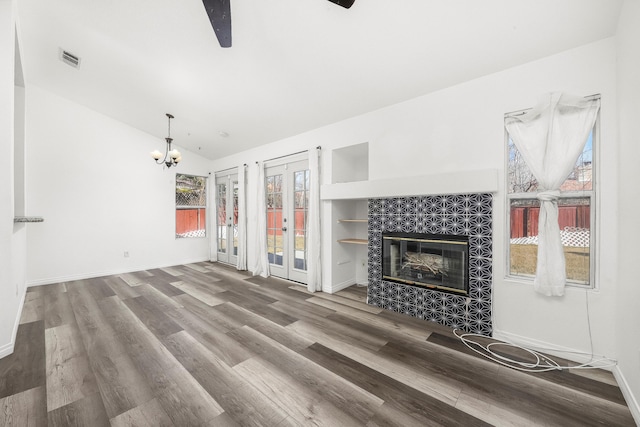 unfurnished living room with a tile fireplace, wood-type flooring, lofted ceiling, a chandelier, and french doors