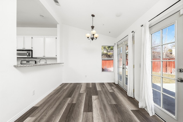 unfurnished dining area featuring vaulted ceiling, sink, a chandelier, dark wood-type flooring, and french doors