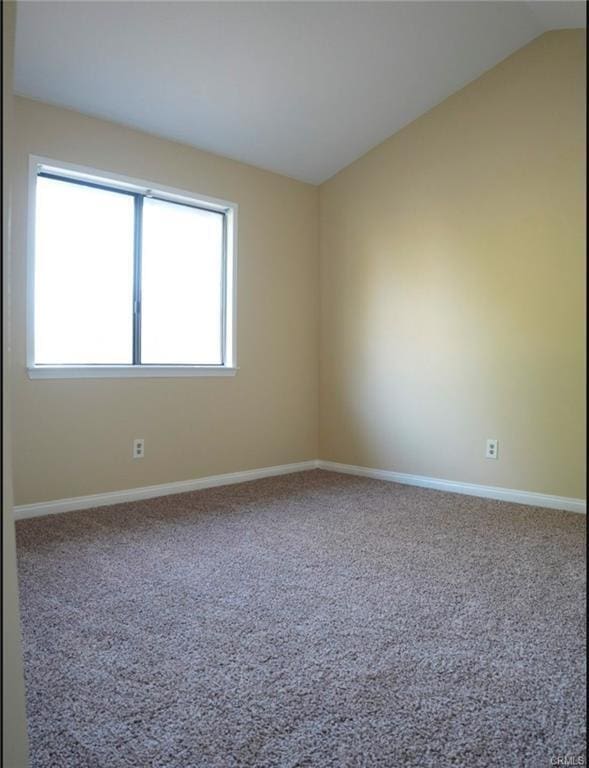 carpeted empty room featuring baseboards, vaulted ceiling, and plenty of natural light