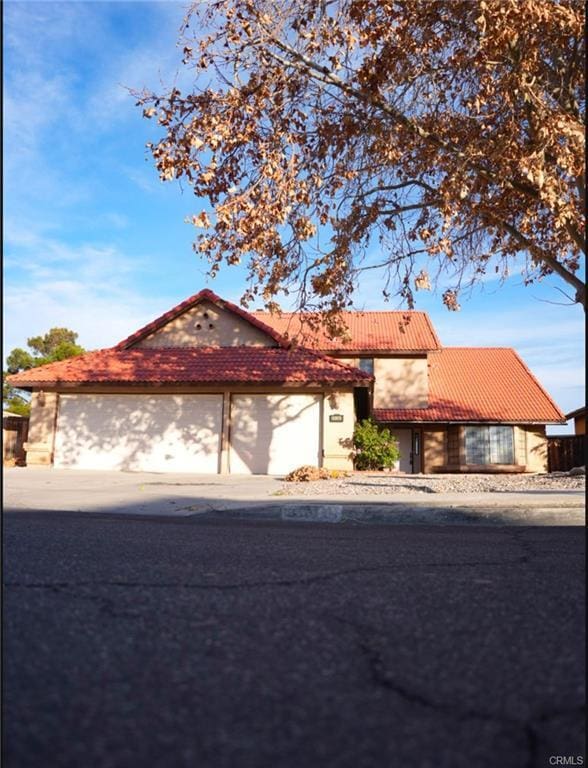 view of front of house featuring an attached garage, driveway, a tiled roof, and stucco siding