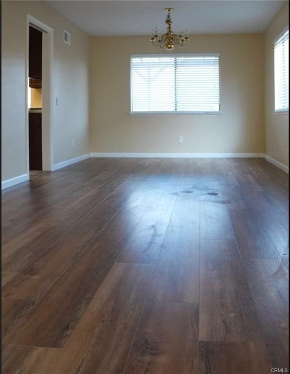 empty room featuring baseboards, visible vents, a chandelier, and dark wood finished floors