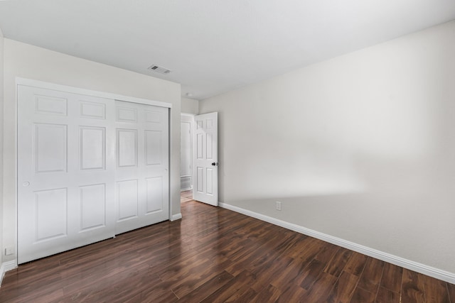 unfurnished bedroom featuring visible vents, baseboards, dark wood-style floors, and a closet
