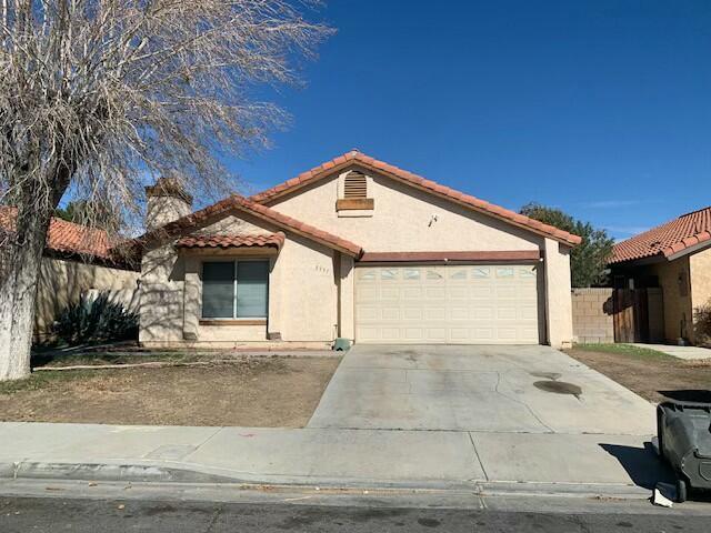 view of front of property with stucco siding, an attached garage, fence, driveway, and a tiled roof