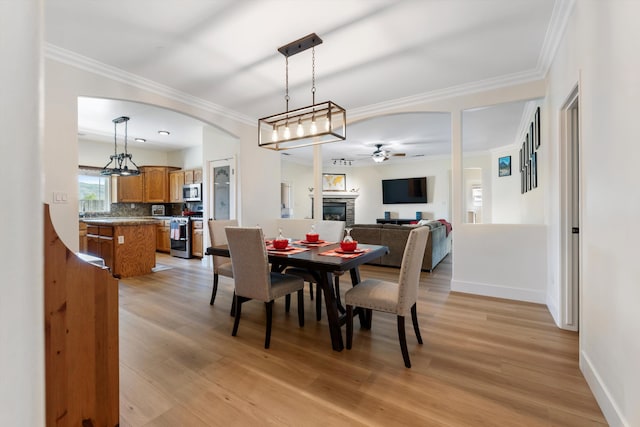dining space featuring ceiling fan, a fireplace, baseboards, light wood-style flooring, and arched walkways