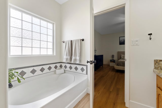 ensuite bathroom with vanity, a garden tub, and wood finished floors
