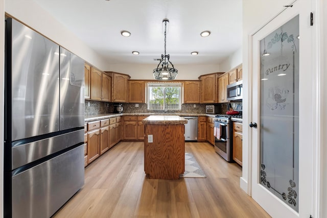 kitchen featuring appliances with stainless steel finishes, light wood-style floors, tasteful backsplash, hanging light fixtures, and a center island