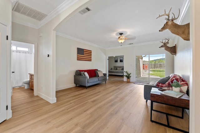 living room featuring light wood-type flooring, ornamental molding, arched walkways, and baseboards