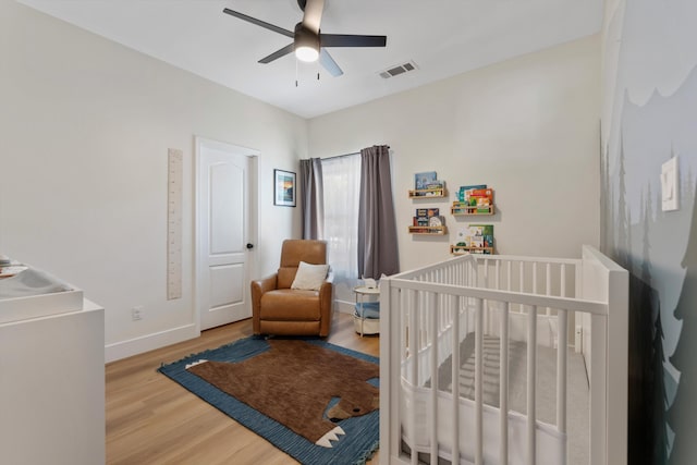 bedroom featuring wood finished floors, a crib, baseboards, and ceiling fan