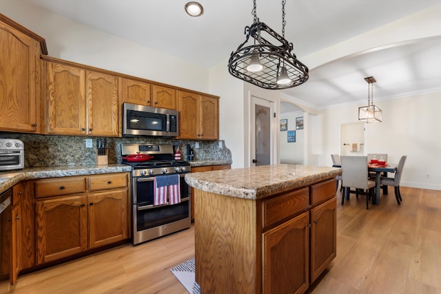 kitchen with stainless steel appliances, arched walkways, decorative backsplash, and brown cabinets