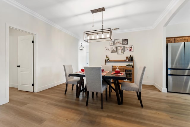 dining area featuring light wood-style flooring, ornamental molding, baseboards, and arched walkways