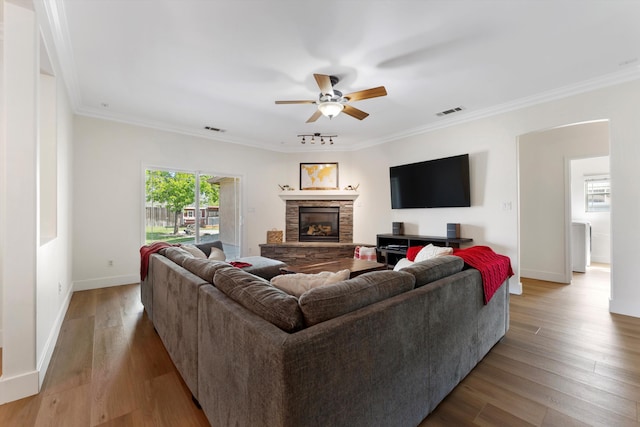 living room featuring a ceiling fan, a fireplace, baseboards, crown molding, and wood finished floors