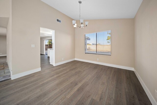 empty room featuring dark hardwood / wood-style floors, lofted ceiling, and an inviting chandelier