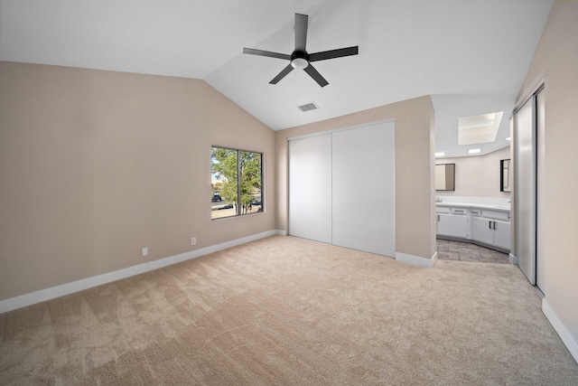 unfurnished bedroom featuring lofted ceiling, light carpet, ensuite bath, ceiling fan, and a closet