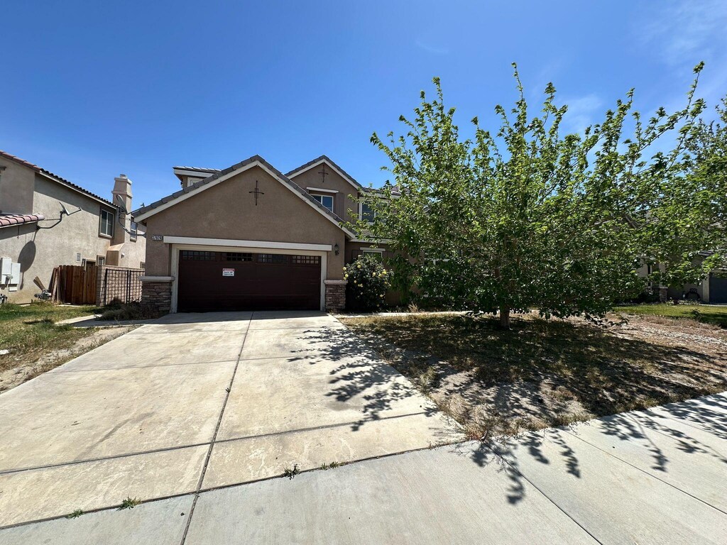 view of side of home featuring a garage, stucco siding, driveway, and stone siding