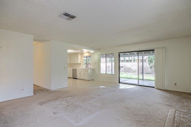 unfurnished living room with a textured ceiling, visible vents, and light colored carpet