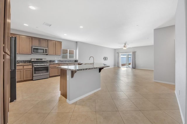 kitchen featuring light stone countertops, appliances with stainless steel finishes, a breakfast bar, ceiling fan, and a center island with sink