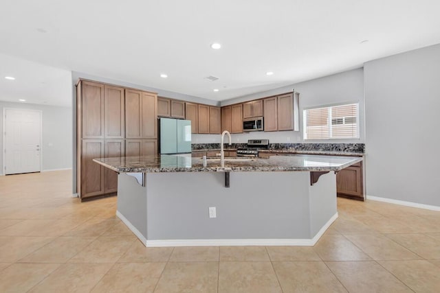 kitchen featuring sink, dark stone counters, a breakfast bar area, a kitchen island with sink, and appliances with stainless steel finishes