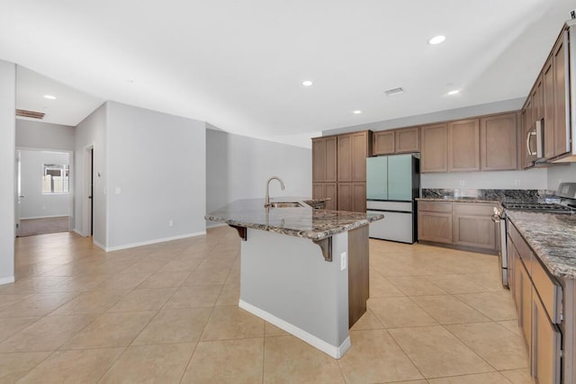 kitchen featuring a center island with sink, sink, dark stone countertops, a kitchen bar, and stainless steel appliances