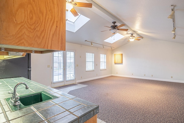 kitchen featuring lofted ceiling with skylight, black refrigerator, tile countertops, sink, and carpet