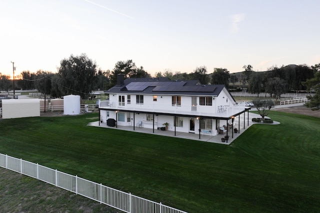 back of property featuring roof mounted solar panels, a lawn, a chimney, and a patio