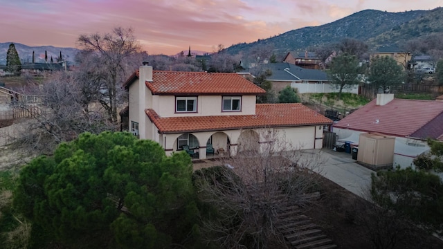 back of house at dusk with driveway, a tile roof, a chimney, an attached garage, and a mountain view