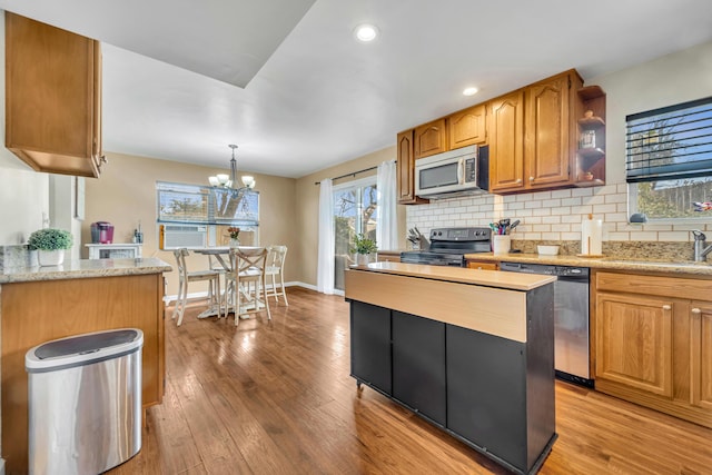 kitchen with stainless steel appliances, a sink, baseboards, light wood-style floors, and backsplash