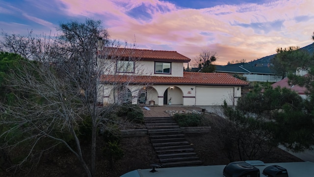 view of front of house featuring a tile roof, stucco siding, an attached garage, driveway, and stairs