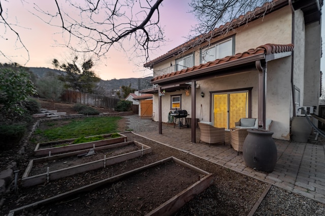 rear view of property featuring a patio area, a garden, fence, and a tiled roof