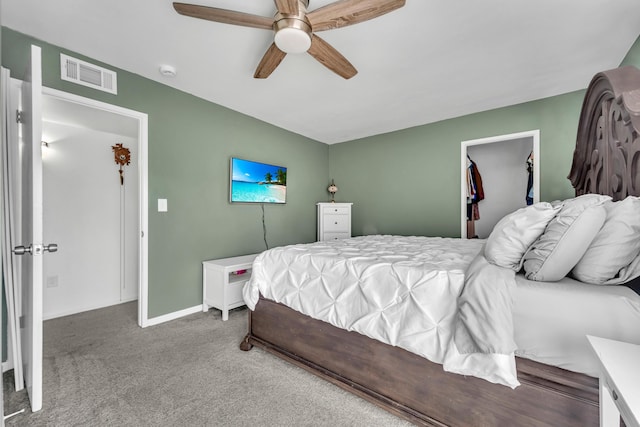 carpeted bedroom featuring ceiling fan, visible vents, a walk in closet, and baseboards