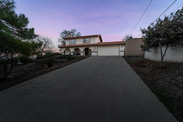 mediterranean / spanish-style home with a garage, concrete driveway, a chimney, a tiled roof, and stucco siding