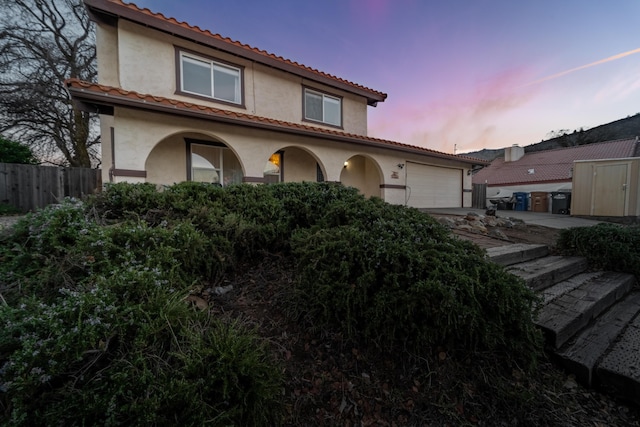 mediterranean / spanish house featuring an attached garage, a tiled roof, fence, and stucco siding