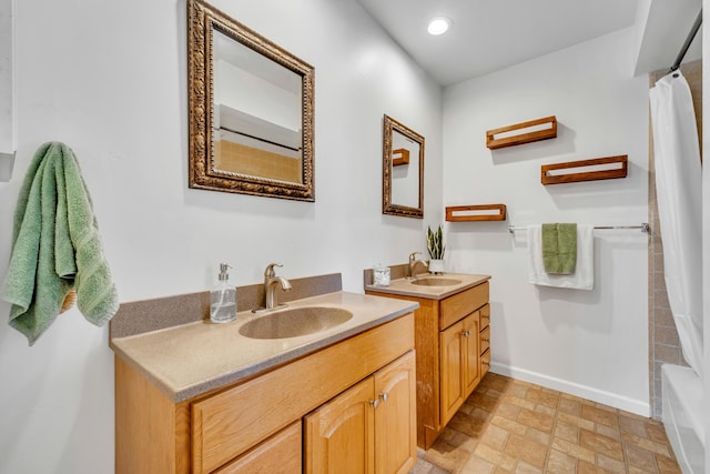 full bathroom with stone finish floor, two vanities, a sink, and baseboards