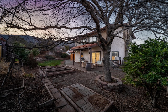 rear view of house featuring stucco siding, a patio area, fence, a garden, and a tiled roof