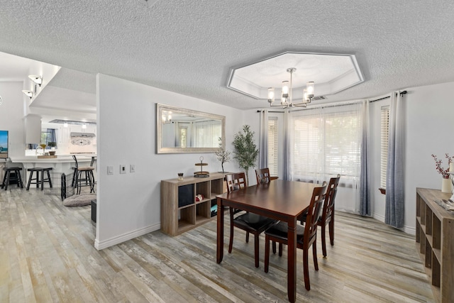 dining area with a wealth of natural light, light hardwood / wood-style floors, a textured ceiling, and an inviting chandelier