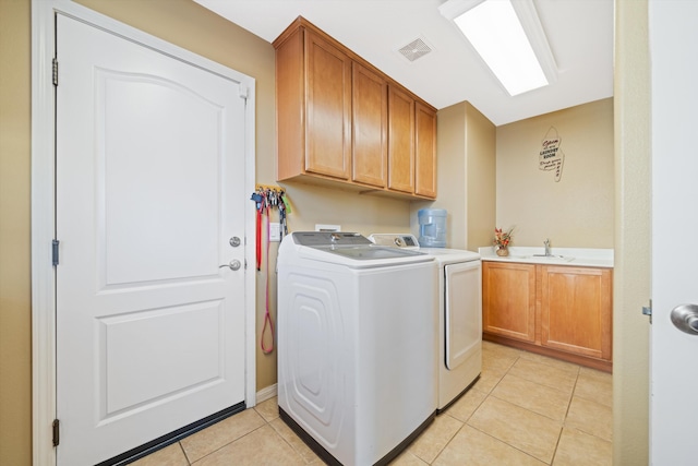 laundry area with washing machine and clothes dryer, sink, cabinets, a skylight, and light tile patterned floors