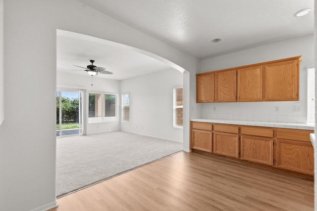 4349 Bethpage Dr, Palmdale, CA 93551 - kitchen featuring light wood finished floors, a ceiling fan, arched walkways, open floor plan, and brown cabinetry