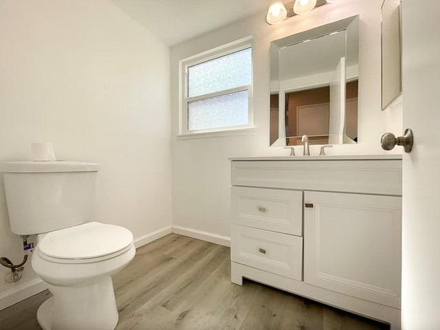 half bath with toilet, vanity, baseboards, and wood finished floors