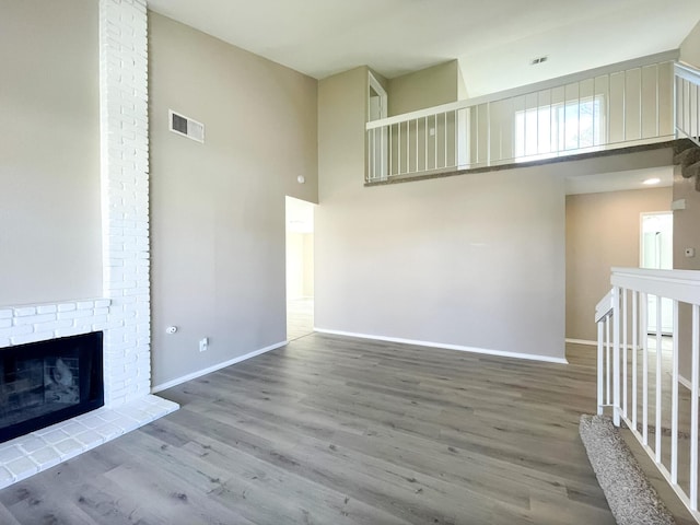 unfurnished living room featuring a brick fireplace, wood finished floors, baseboards, and a towering ceiling