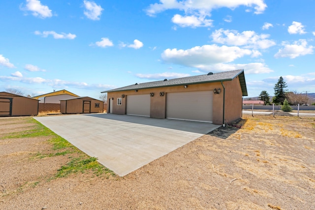 view of front of property featuring stucco siding, a shed, fence, and an outbuilding