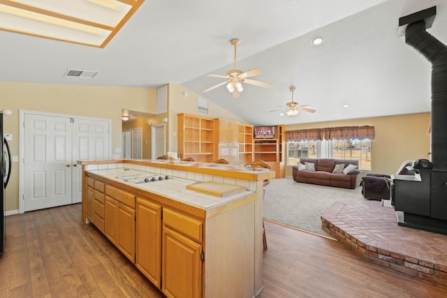 kitchen featuring dark wood-type flooring, visible vents, vaulted ceiling, tile counters, and a wood stove