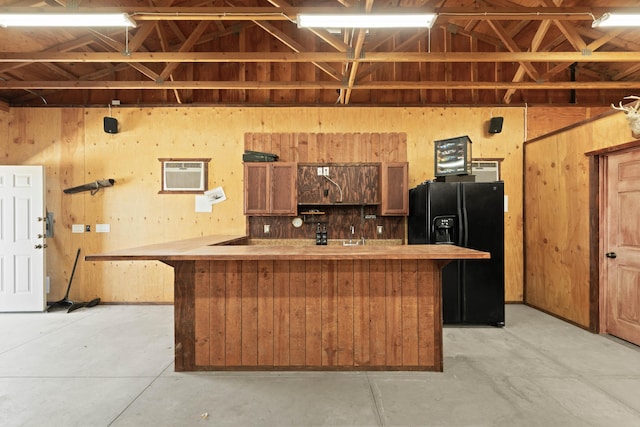 kitchen with lofted ceiling, an AC wall unit, black fridge with ice dispenser, and concrete flooring