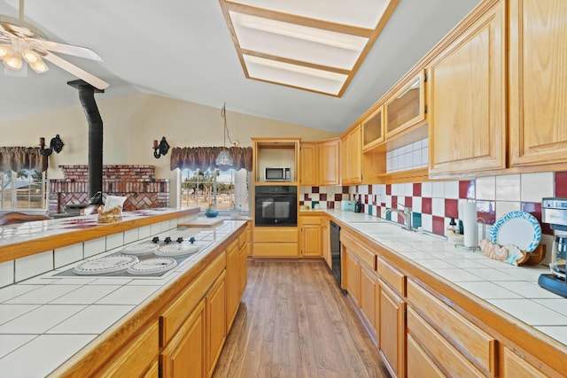 kitchen with tile counters, decorative backsplash, vaulted ceiling, light wood-type flooring, and black appliances