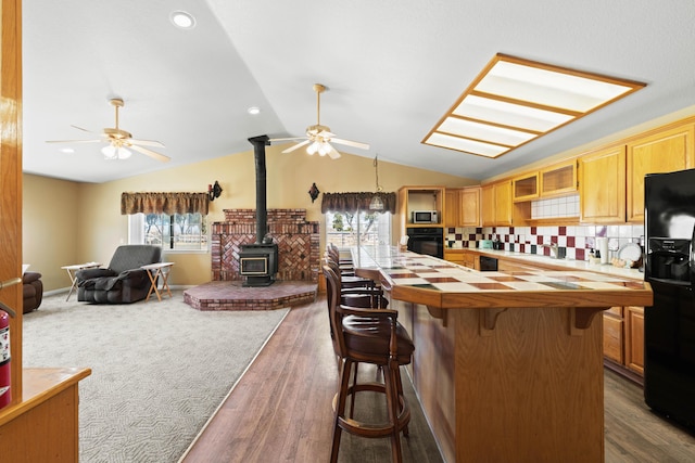 kitchen with tile countertops, a breakfast bar area, a ceiling fan, vaulted ceiling, and black appliances